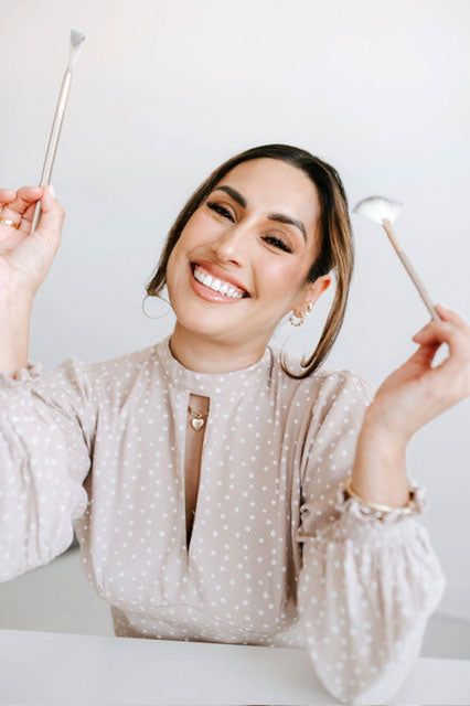 Aesti Amy holding two facial brushes on a white background
